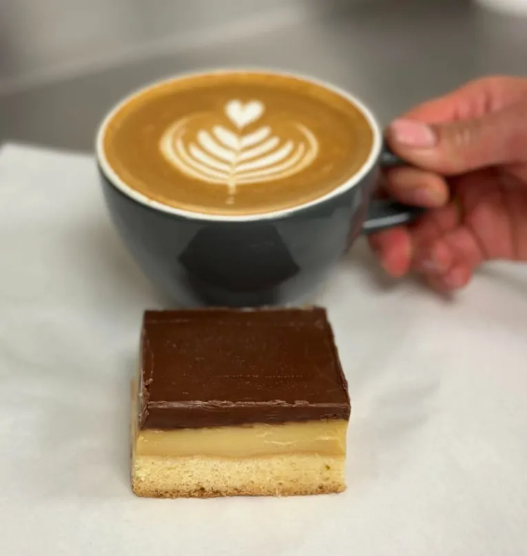 Flat white with latte art next to a caramel slice