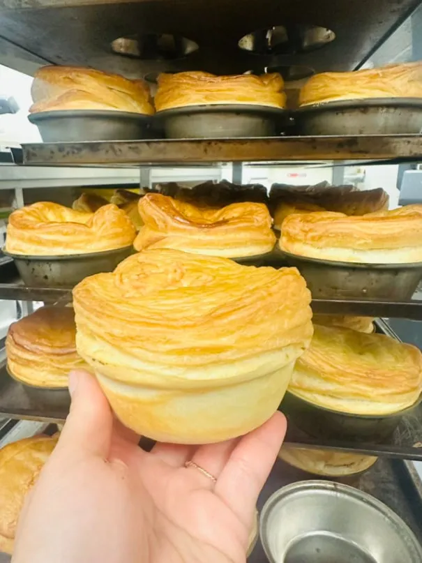 A freshly baked pie held up in front of a rack of pies